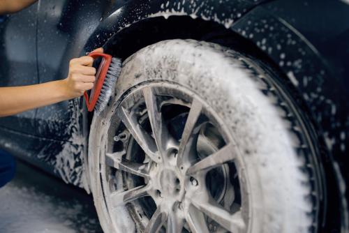 Female washer with brush cleans wheel, car wash