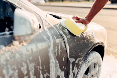 Male hand rubbing the car with foam, carwash